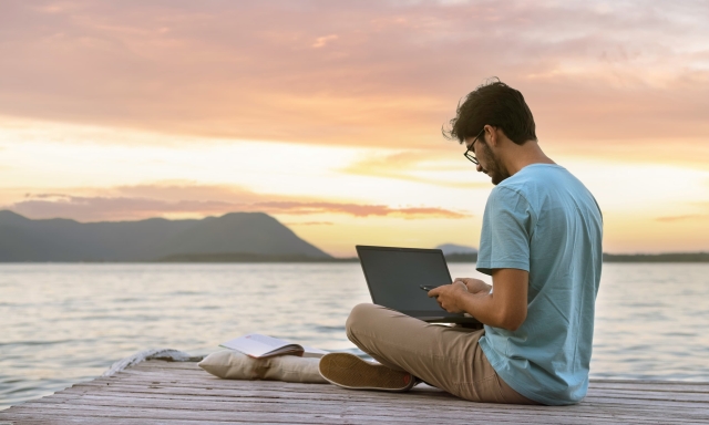 Image of a man sitting on a deck with a laptop